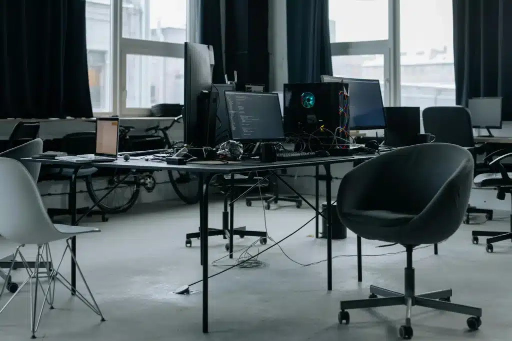 Disorganized office workspace with multiple computers and cables symbolizing complex IT systems hindering business efficiency