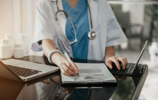 Doctor working on laptop computer and tablet and medical on clipboard on desk, electronics medical record system EMRs concept.
